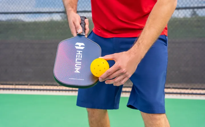 Player holding a Helium pickleball paddle and ball on court, sporting goods photography